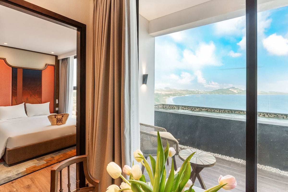 Ein Hotelzimmer mit Bett, Meerblick und einem Balkon mit Tisch und Stühlen.