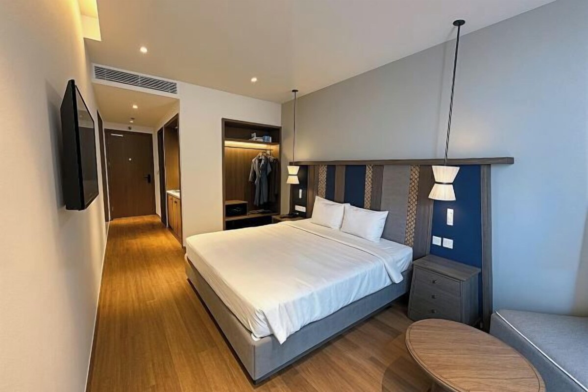 Una habitación de hotel moderna con una cama grande, una mesita de noche, un armario y un televisor montado en la pared.