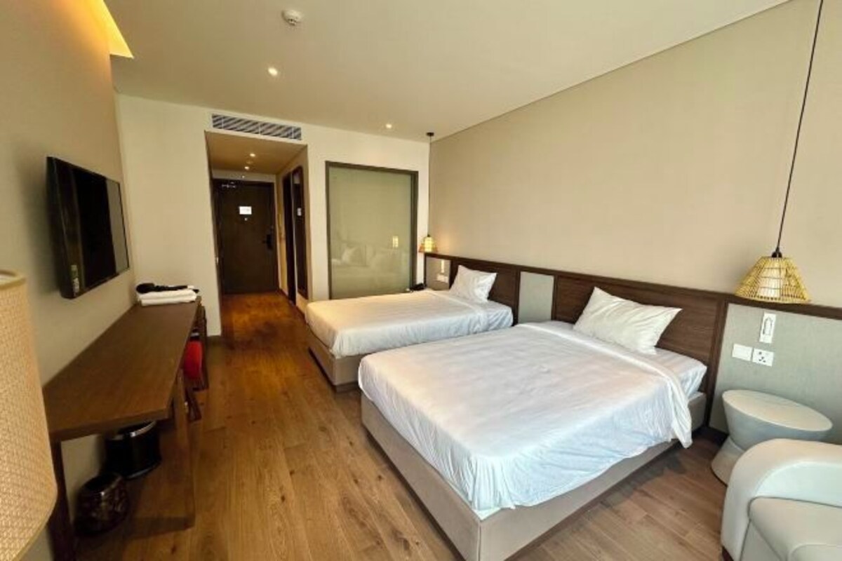 A hotel room with two beds, a desk, a chair, a TV, and a bathroom.