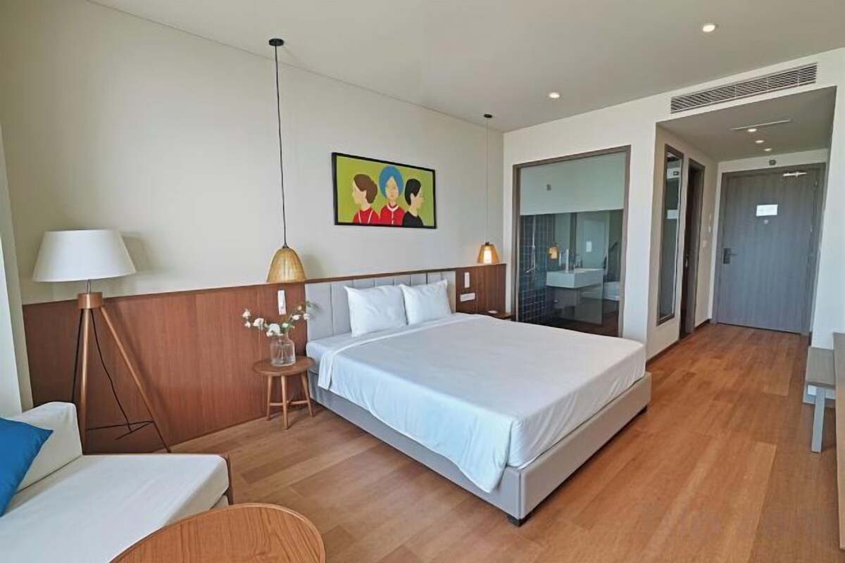 Ein Hotelzimmer mit einem großen Bett, Nachttischen, einer Lampe, einem kleinen Tisch mit Blumen und einem Bild an der Wand.