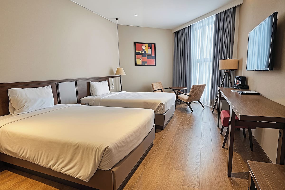 Ein Hotelzimmer mit zwei Betten, einem Schreibtisch, einem Stuhl, einem Fernseher und einem Bild an der Wand.