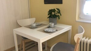 Una zona de dinar petita amb taula, cadires, una planta en test i un calendari penjat a la paret.