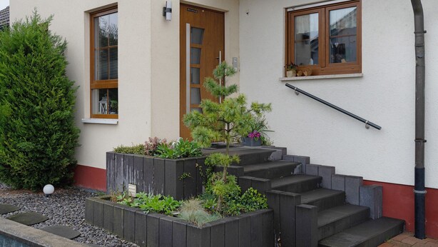 A building with a staircase leading to a door, a window with a view, and a small garden area with plants. - Apartment 'Sigrid' with Shared Garden, Balcony and Wi-Fi (Forchheim)
