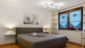 A bedroom with a bed, bedside lamps, a window with curtains, a radiator, and a wall-mounted light fixture. - Apartment 'Sigrid' with Shared Garden, Balcony and Wi-Fi (Forchheim)