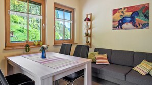 A room with a dining table, chairs, a sofa, a window with a view of greenery, and a painting on the wall. - Apartment '1, 45qm' with Mountain View, Shared Terrace and Wi-Fi (Oberwolfach)