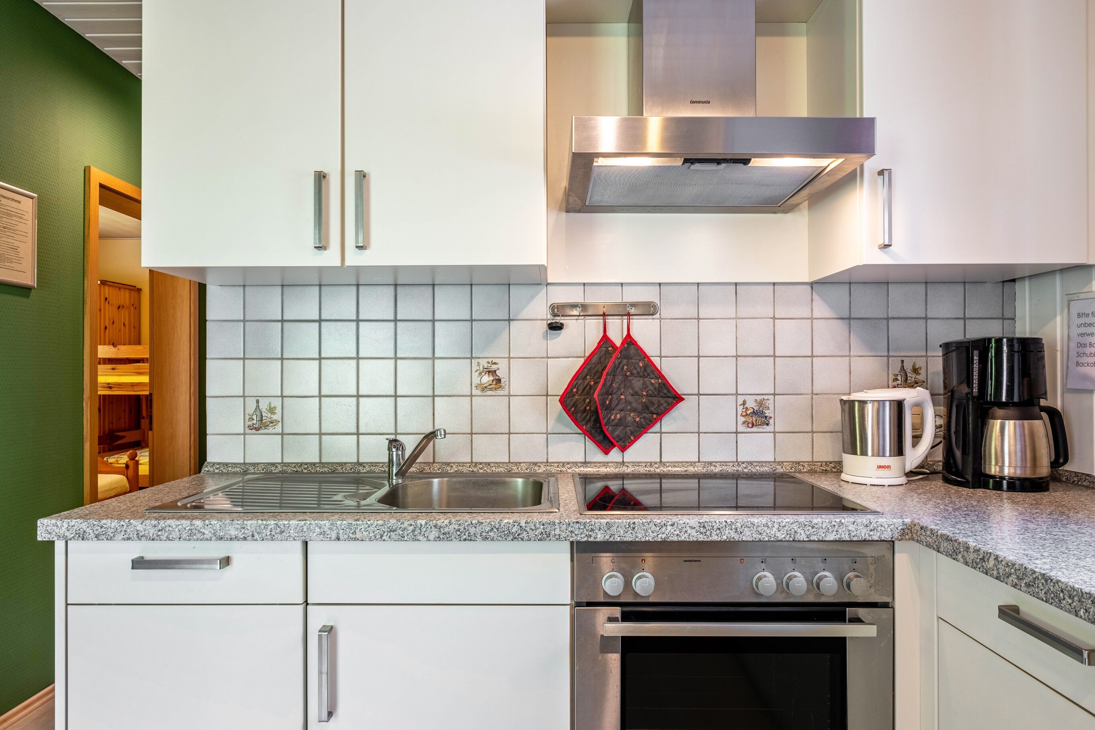 Een keuken met witte kastjes, een roestvrijstalen afzuigkap, een ingebouwde oven, een koffiezetapparaat en een waterkoker.