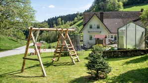 A house with a red-tiled roof, a wooden swing set, and a greenhouse. - Apartment '2, 45qm' with Mountain View, Shared Terrace and Wi-Fi (Oberwolfach)