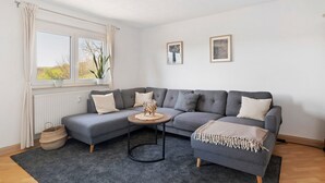 Un salon moderne avec un canapé d’angle gris, une table basse ronde et un tapis gris.