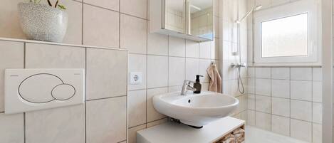 A modern bathroom with a white sink, a mirror, a shower, and a potted plant.