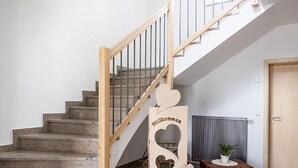 Una escalera con barandilla de madera, un letrero de bienvenida de madera, un radiador y una planta en maceta.