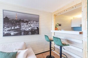 A room with a large cityscape photo, a sofa, two bar stools, and a kitchen area. - Apartment 'Schwarzwaldtraum 4' with Private Terrace, Shared Garden and Wi-Fi (Sasbachwalden)