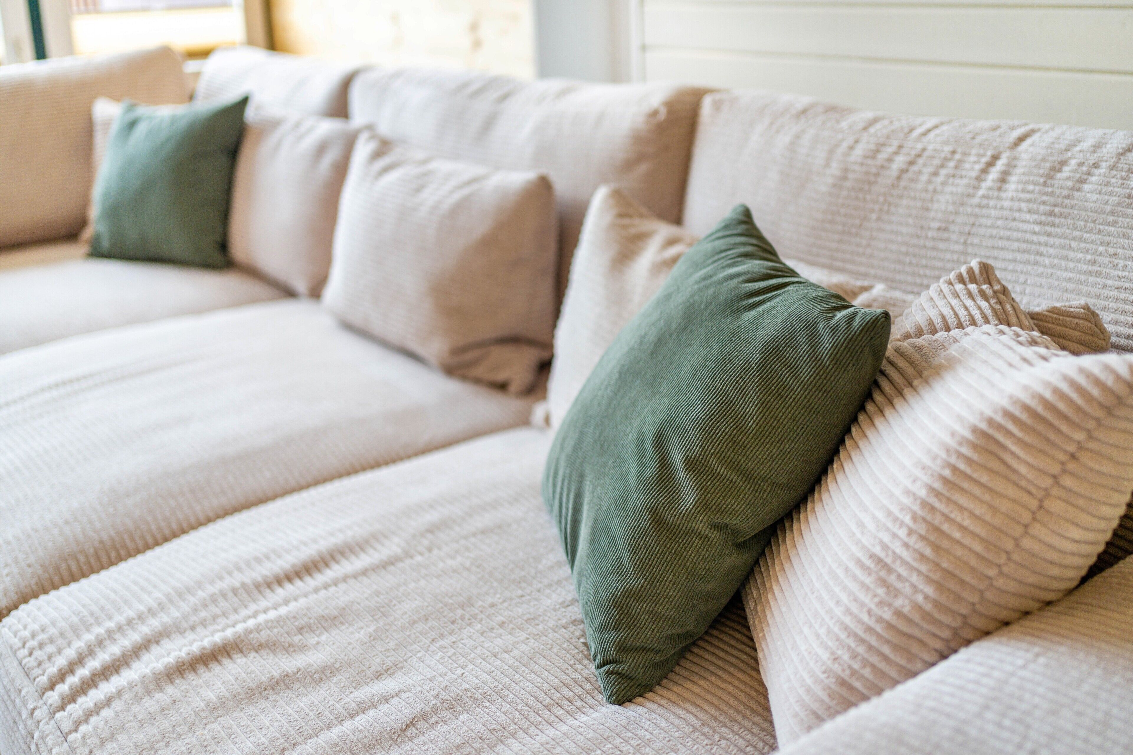 A beige sofa with multiple cushions, including a green one, in a well-lit room.