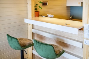 A compact kitchenette with a countertop, two green chairs, a potted plant, and a wooden wall. - Apartment 'Schwarzwaldtraum 4' with Private Terrace, Shared Garden and Wi-Fi (Sasbachwalden)