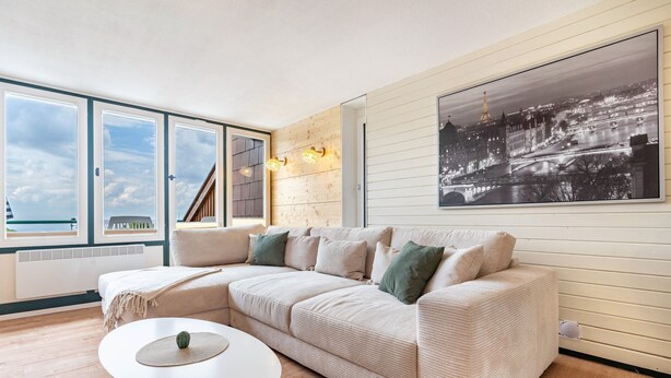 A modern living room with a sectional sofa, a round coffee table, and a large window with a view of a cityscape.