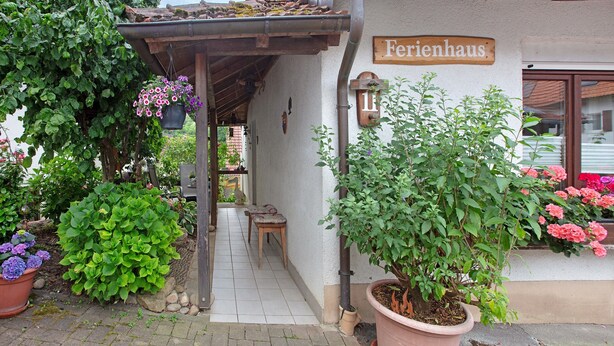 A building named 'Ferrenhaus' with a covered outdoor area, potted plants, and a tiled pathway. - Holiday Home 'Am Blumengässle' with Balcony and Wi-Fi (Müllheim im Markgräflerland)