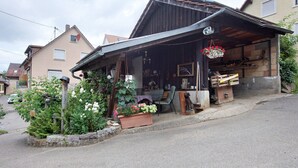 A rustic wooden building with a covered porch, a flower bed, and various items displayed outside. - Holiday Home 'Am Blumengässle' with Balcony and Wi-Fi (Müllheim im Markgräflerland)