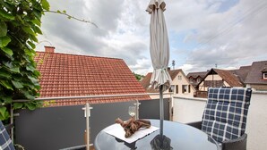 A round glass table with a white cloth, a glass of wine, and a decorative item on it. There are two wicker chairs with blue and white checkered cushions. - Holiday Home 'Am Blumengässle' with Balcony and Wi-Fi (Müllheim im Markgräflerland)