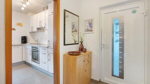 A modern kitchen with white cabinets, a built-in oven, and a wooden cabinet with a vase. - Holiday Home 'Am Blumengässle' with Balcony and Wi-Fi (Müllheim im Markgräflerland)