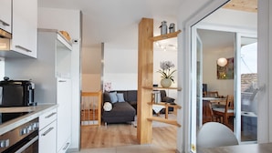 Una cocina moderna con electrodomésticos integrados, un comedor con mesa y sillas de madera, y una sala de estar con sofá y planta en maceta.