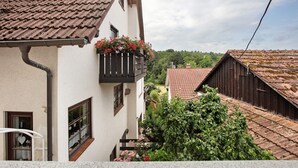 Un edificio tradicional con techo de tejas, un balcón con flores y vistas a un área boscosa.