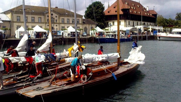 A wooden boat docked at a marina with people on board, a building with a red roof in the background, and another boat named 'Austria' in the distance. - Holiday Apartment 'K3ab, 60sqm' with Balcony and Wi-Fi (Konstanz)