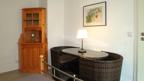 A room with a wicker chair, a small table with a lamp, a wooden cabinet, and a framed picture on the wall. - Holiday Apartment 'K3ab, 60sqm' with Balcony and Wi-Fi (Konstanz)