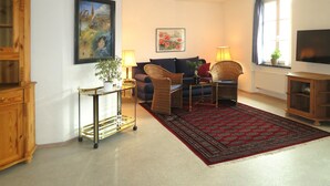 A living room with a sofa, two side tables, a TV, a large painting, and a window with curtains. - Holiday Apartment 'K3ab, 60sqm' with Balcony and Wi-Fi (Konstanz)