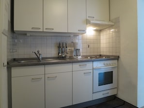 Cozinha com armários brancos, pia de aço inoxidável, cafeteira Bosch e forno embutido.