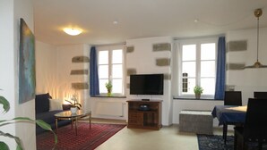 A living room with a sofa, a coffee table, a TV, and a dining area with a table and chairs.