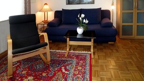 A living room with a sofa, a chair, a coffee table, a lamp, a painting, and a patterned rug. - Apartment 'D2, 60qm' with Private Terrace, Shared Garden and Wi-Fi (Konstanz)