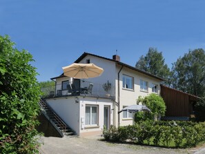 Kaksikerroksinen talo, jossa on parveke, portaikko ja puutarha-alue.