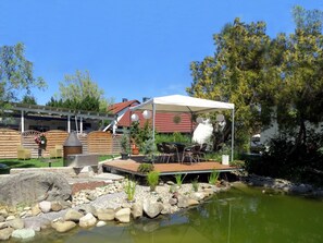 Un jardín con un estanque, mobiliario exterior y una zona cubierta.
