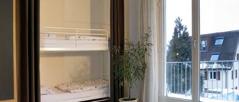 A bedroom with a bunk bed, a potted plant, and a view of the outside.