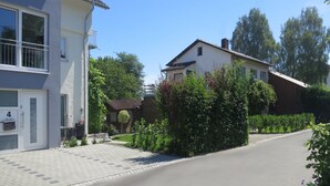 A residential street with houses, a paved driveway, and greenery.