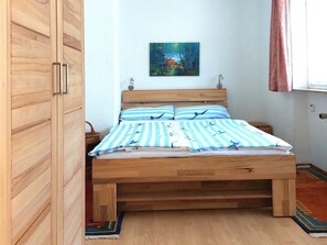 A bedroom with a wooden bed, striped bedding, a painting on the wall, and a window with curtains. - Apartment 'D3, 40qm' with Private Garden and Wi-Fi (Konstanz)