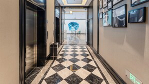 A hotel corridor with a checkered floor, framed artwork on the walls, and a large blue floral mural in the background. - xana Hotel  (Qionghai)