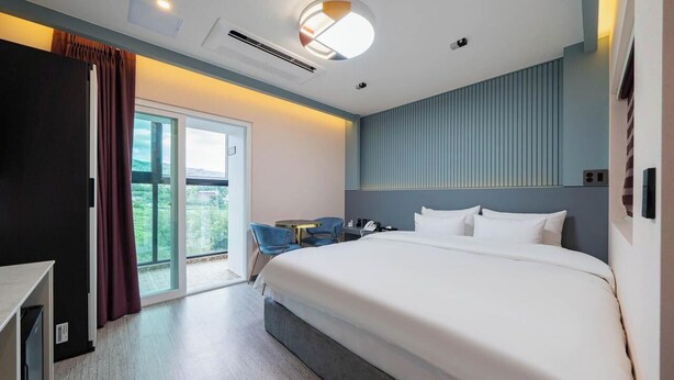 A modern hotel room with a large bed, a desk, a chair, and a view of the outdoors. - peach motel (Wonju)