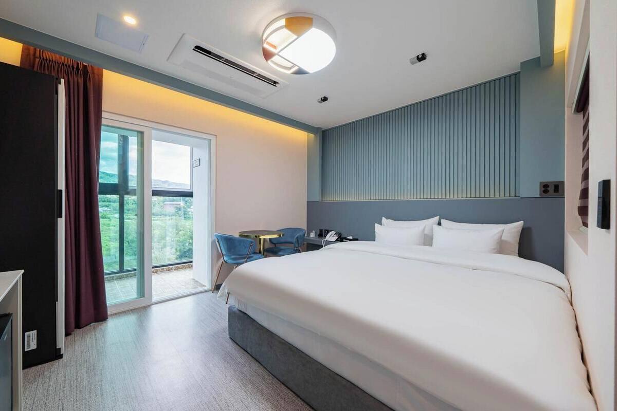 A modern hotel room with a large bed, a desk, a chair, and a view of the outdoors.
