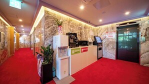 A hotel reception area with a marble wall, a red carpet, a coffee machine, a refrigerator, and a sign indicating a 7-day stay limit. - peach motel (Wonju)