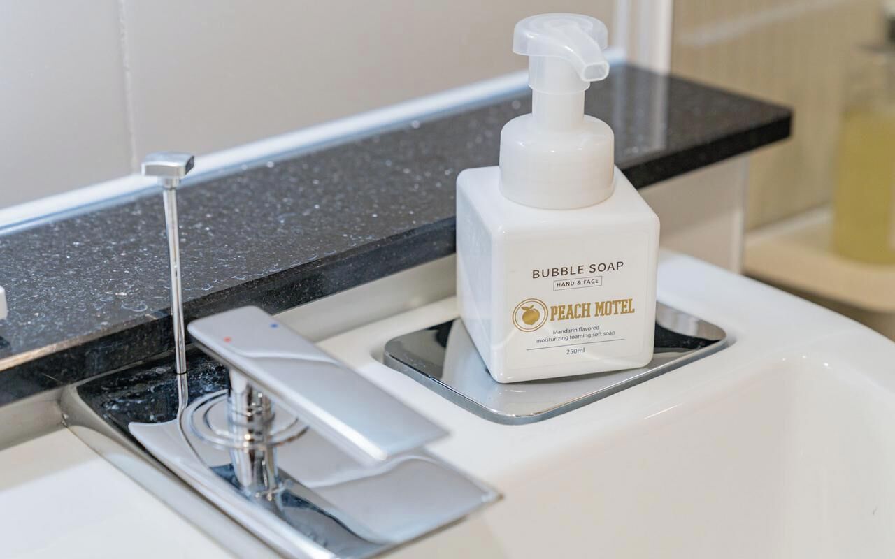 A bathroom sink with a bottle of bubble soap labeled "PEACH MOTEL" and a soap dispenser.