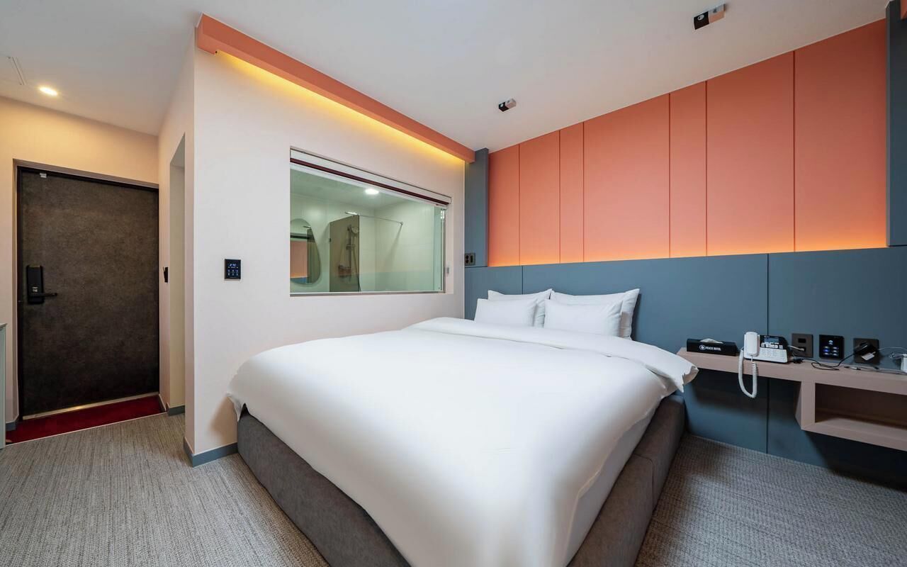 Una habitación de hotel moderna con una cama grande, una mesita de noche con teléfono y un espejo sobre la cama.