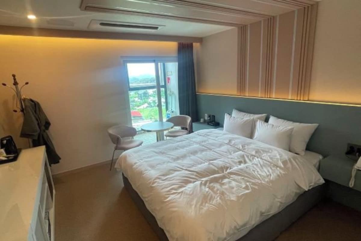A hotel room with a large bed, a small table, a chair, and a view of the outdoors.