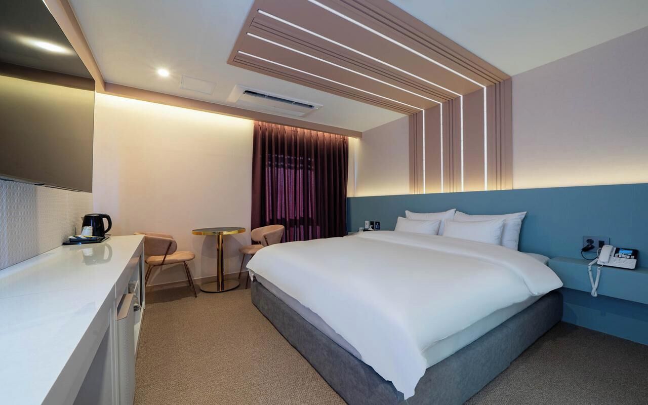 Una habitación de hotel moderna con una cama grande, un escritorio con cafetera, una silla y una mesita.