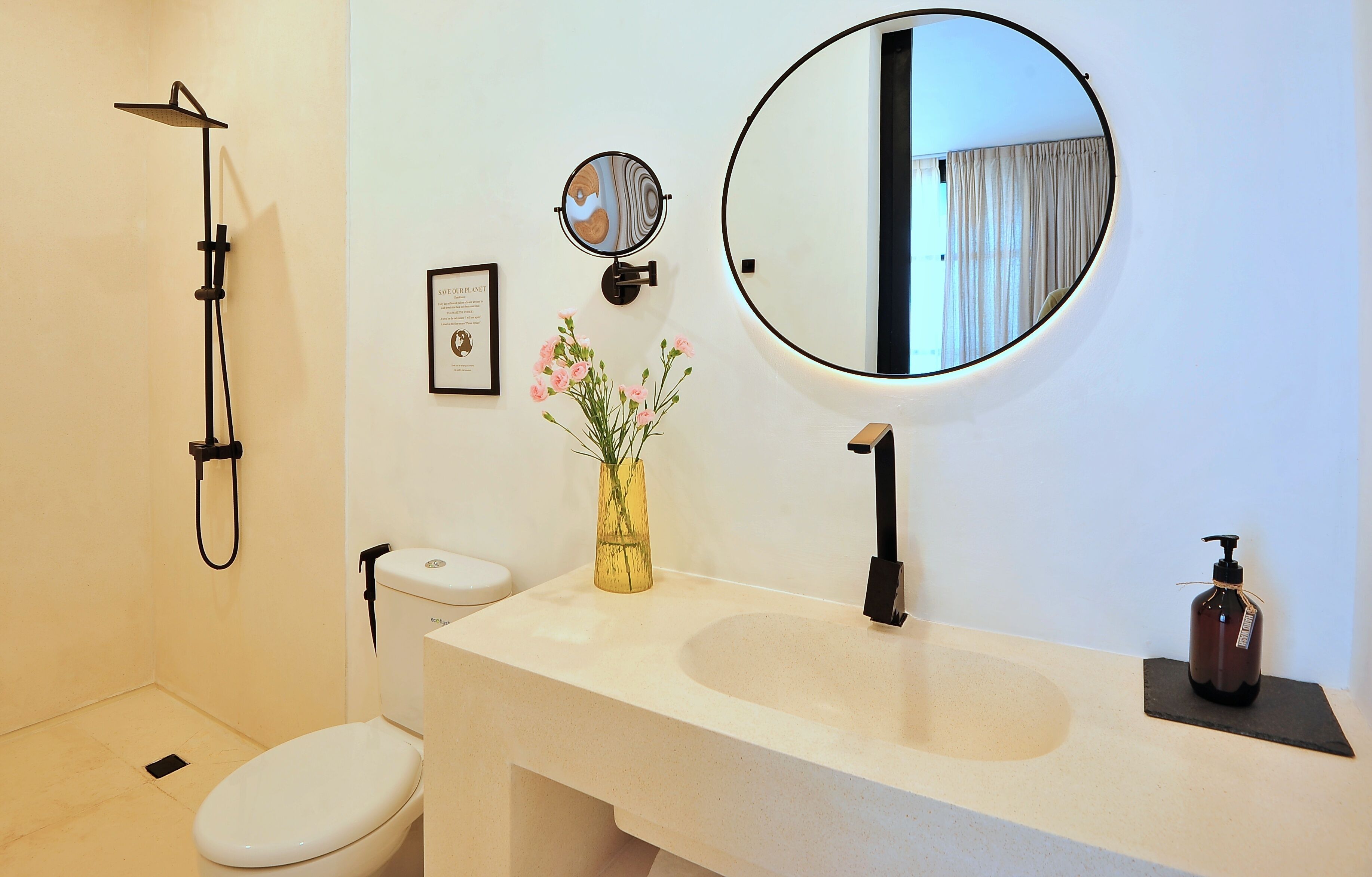 Un baño con inodoro, lavamanos, espejo, ducha y un florero con flores.