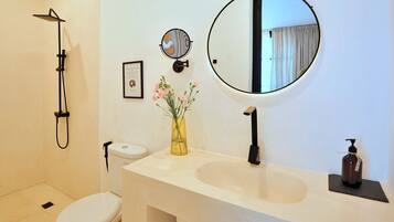 Un baño con inodoro, lavamanos, espejo, ducha y un florero con flores.