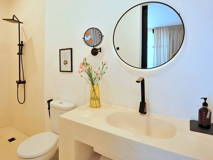 Un baño con inodoro, lavamanos, espejo, ducha y un florero con flores.