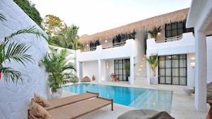 A poolside area with lounge chairs, a pool, and a building with a thatched roof.