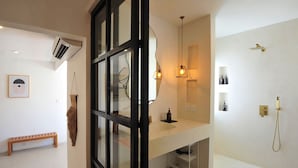 A modern bathroom with a glass door, a white sink, a mirror, a hanging light fixture, and a shower with a handheld showerhead.