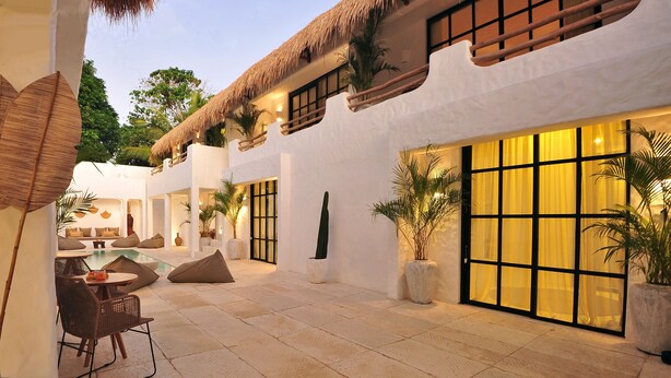 A courtyard with a pool, seating area, and a building with large windows and a thatched roof.