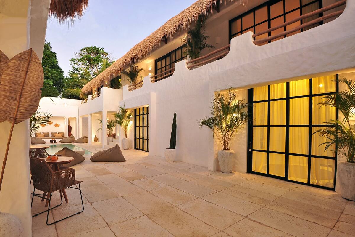 A courtyard with a pool, seating area, and a building with large windows and a thatched roof.